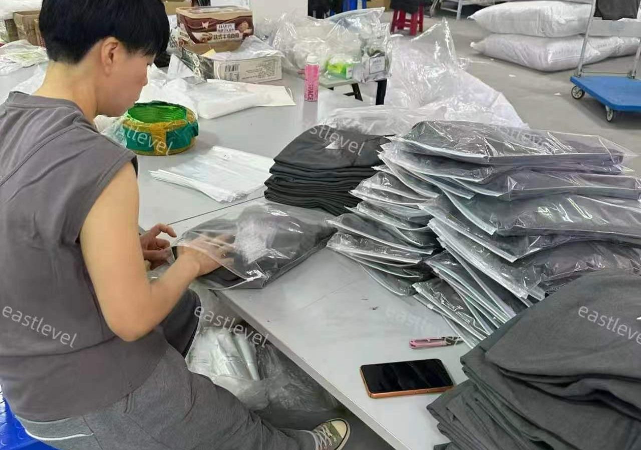 Worker folding and bagging finished garments at a packing table