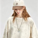 Model wearing the washed cream crewneck with a cap